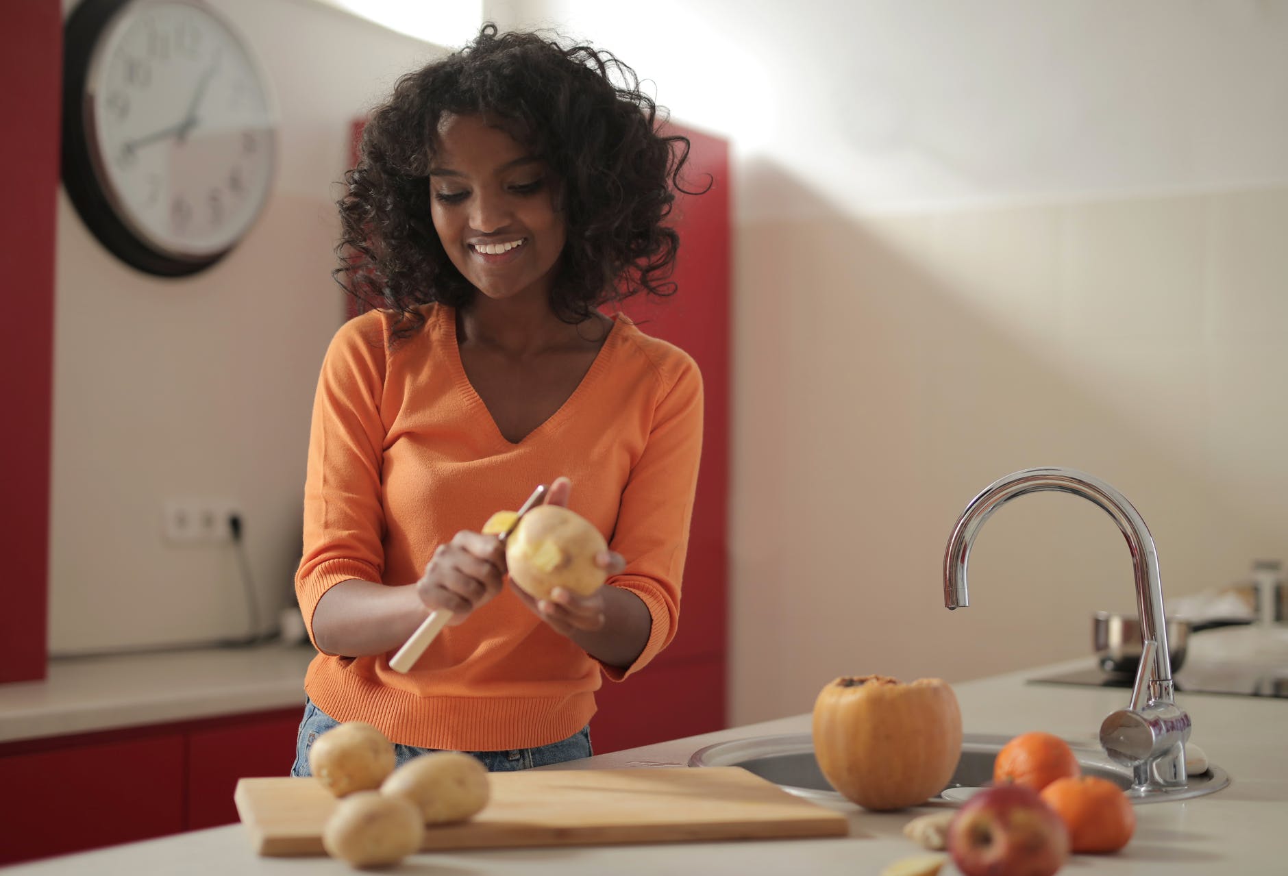 woman in orange long sleeve shirt peeling potato