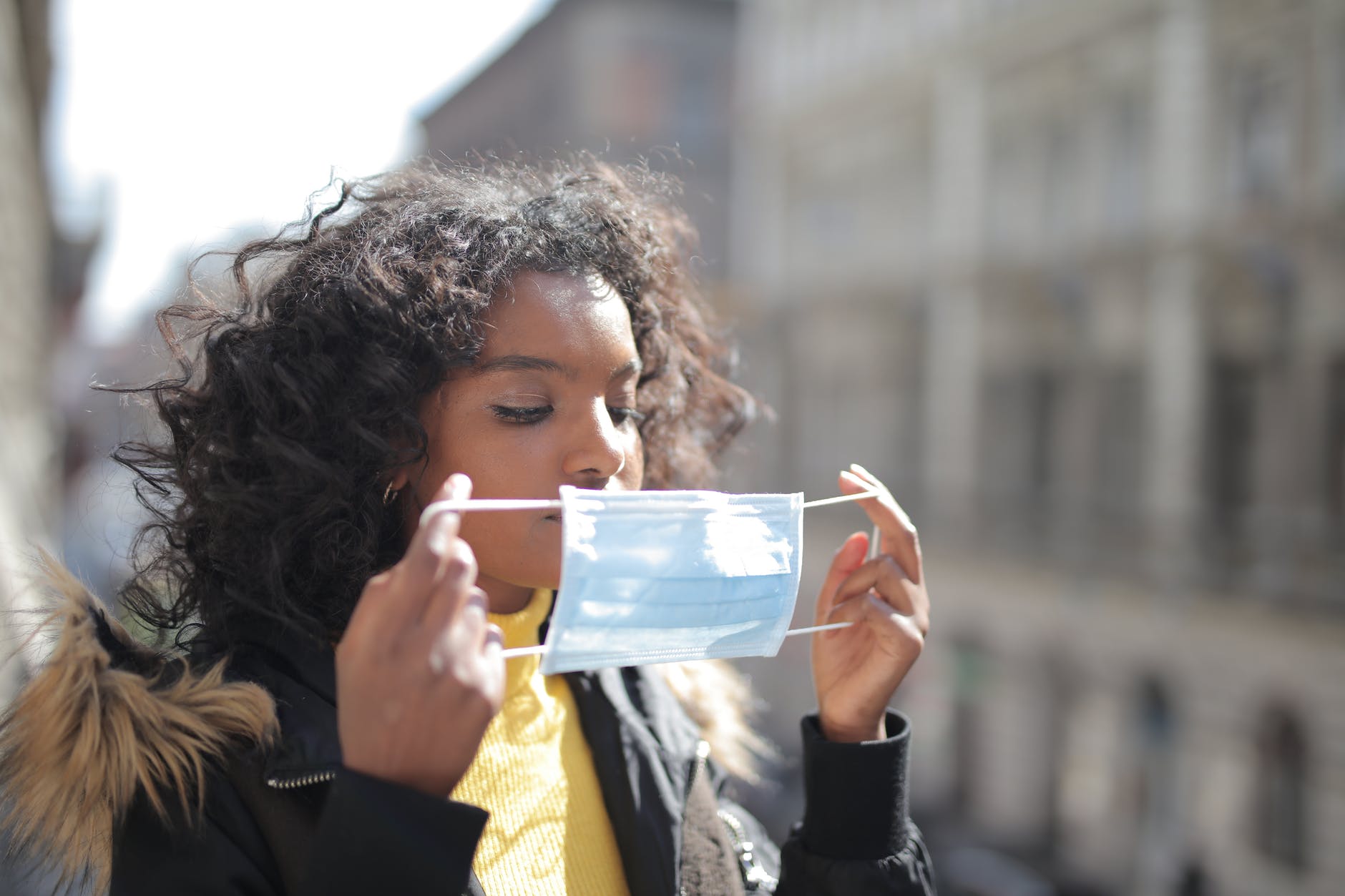 serious young ethnic lady putting on medical mask on street