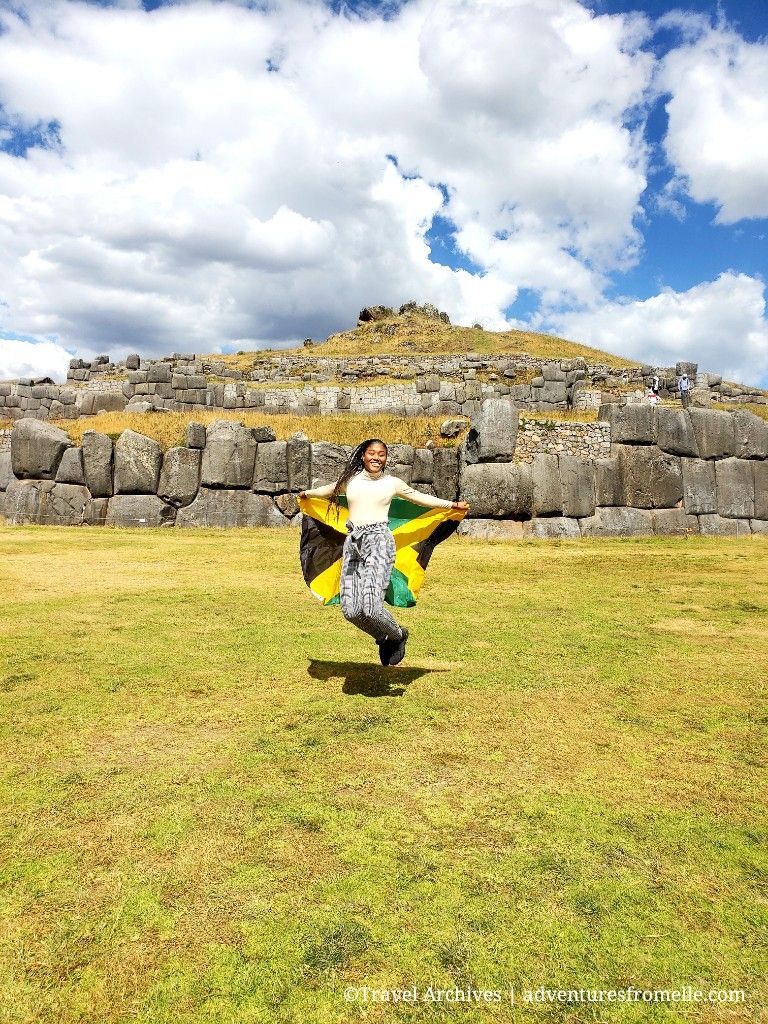 Girl jumps with Jamaican flag in front Sacsayhuaman